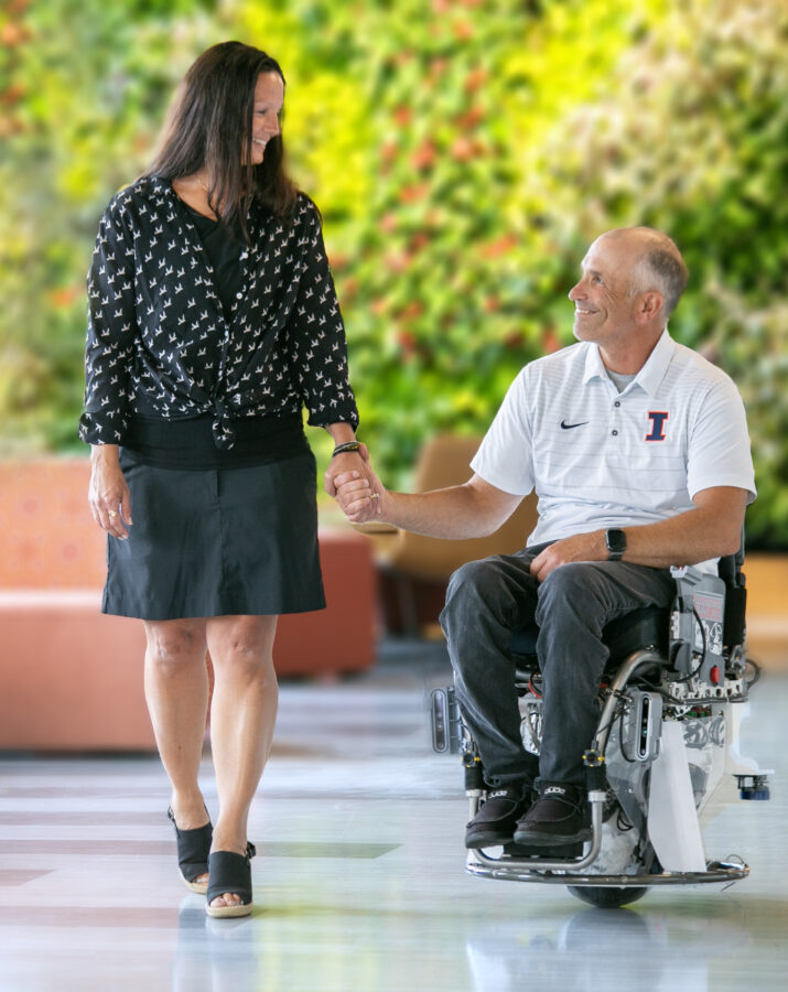 Woman holds the hand of a man in a wheeled device.