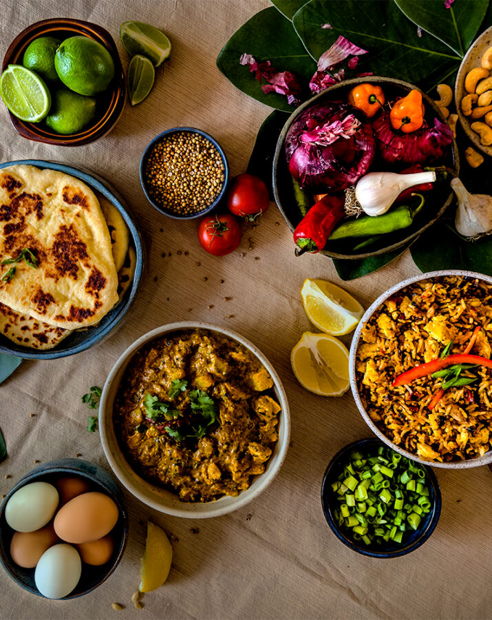 Three recipes in various-sized bowls and ingredients like garlic, peppers, egg, and limes are on a dining table from bird's eye view.