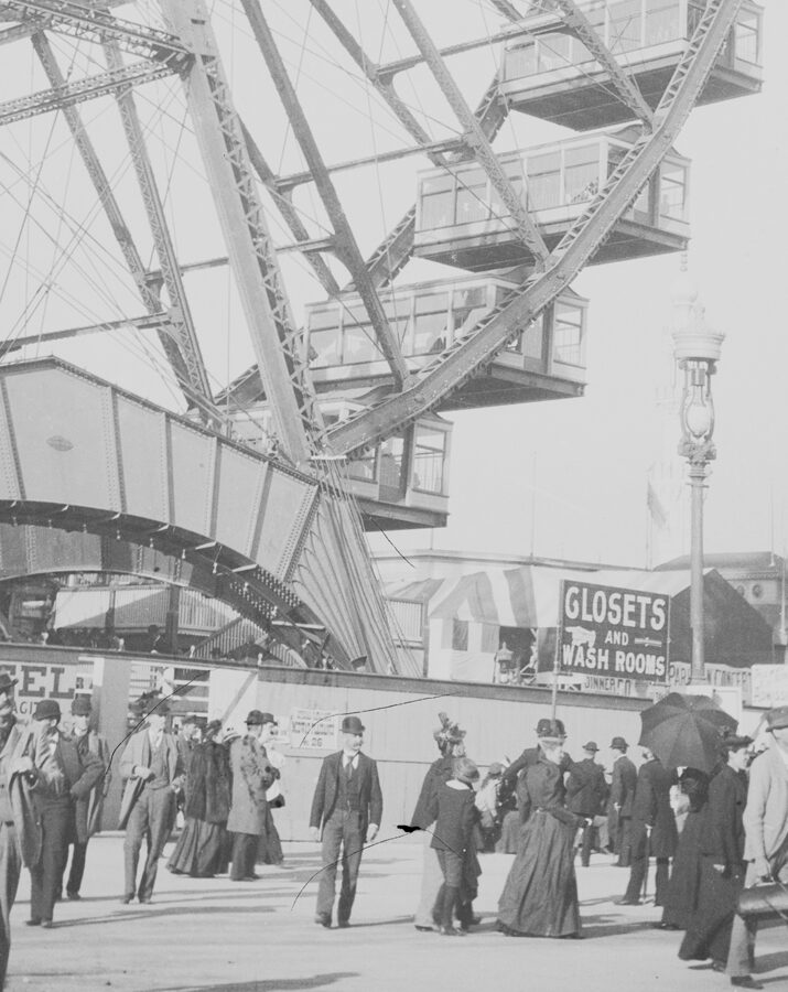 black and white photo of a ferris wheel with patrons walking on the ground in front